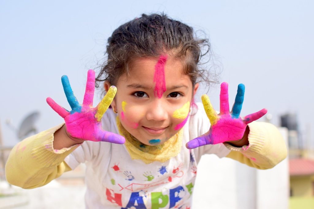 Child celebrating Holi with colourful gulal on hands and face using safe skin-friendly colours